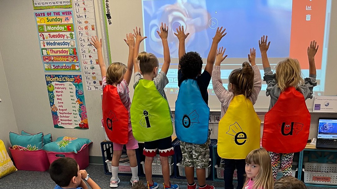 Students practicing their vowels in superhero capes